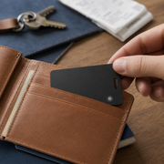 Ultra-thin black tracking card sliding into a tan leather wallet